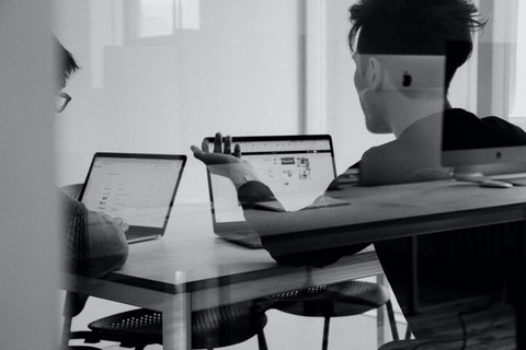 black and white image of people talking while looking at computers